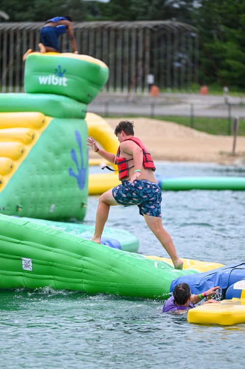 Teenage boy conquers obstacle on Adventure Island, floating water obstacle course, while visiting Bear Paw Adventure Park in the summer.