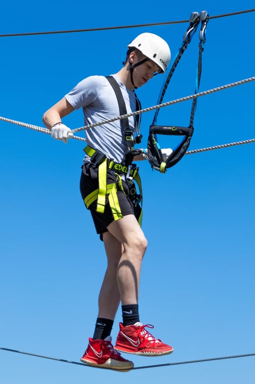 Teenage boy conquers an obstacle on Bear Paw Ropes Course at Bear Paw Adventure Park, on a sunny summer day.