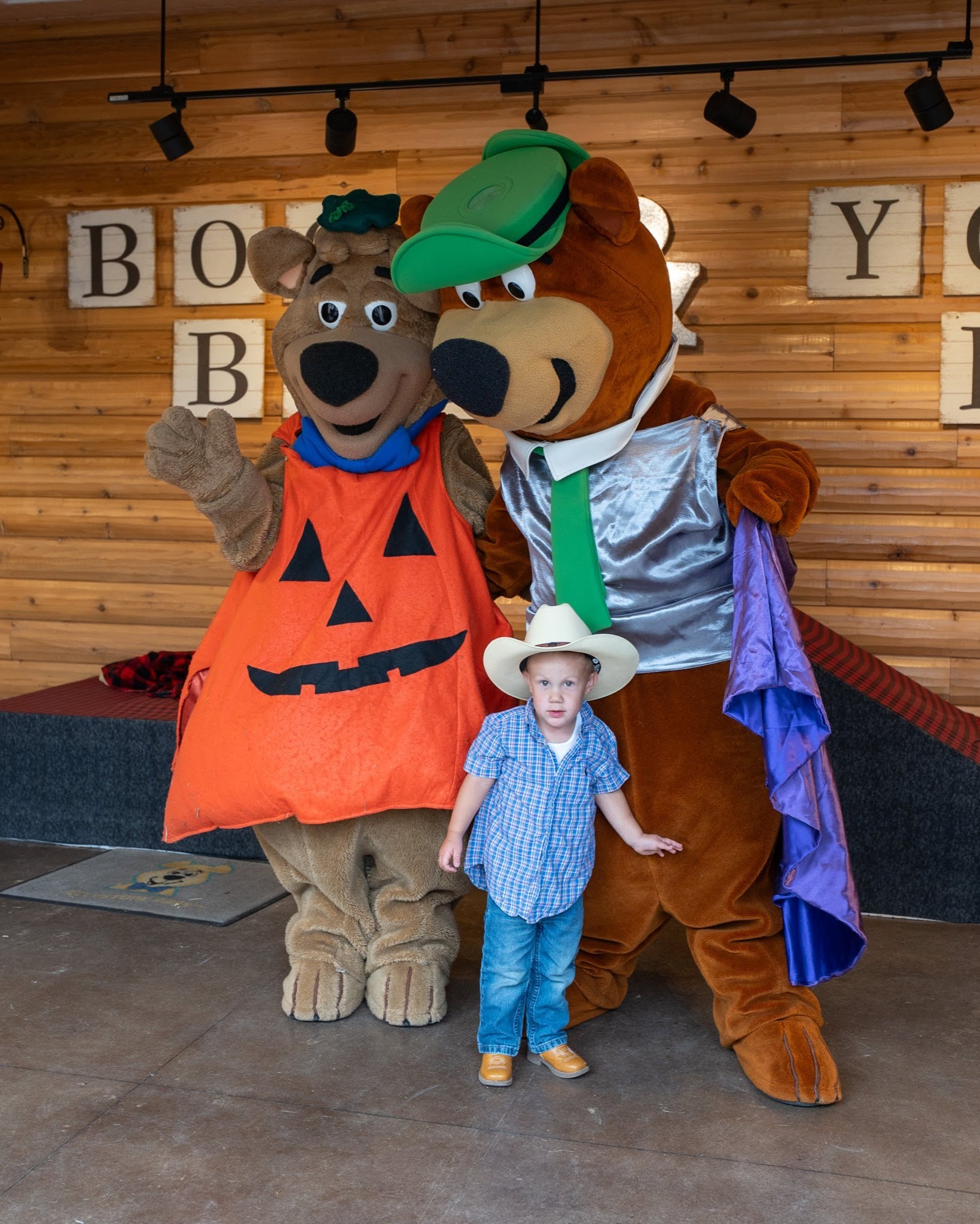 Toddler dressed as a cowboy smiles for a photo with Yogi Bear™ and Boo Boo™ at Jellystone Park™ Caledonia.