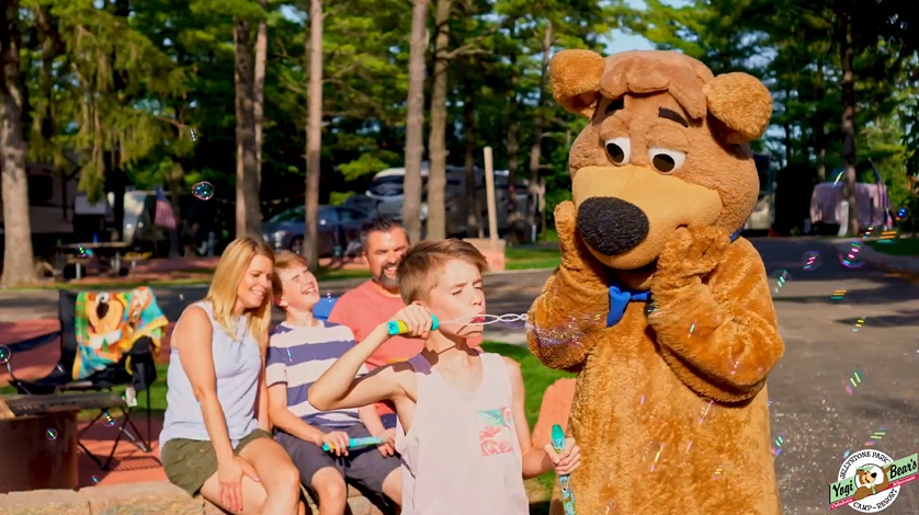 An image of a family camping at Jellystone Park having fun with Boo Boo.