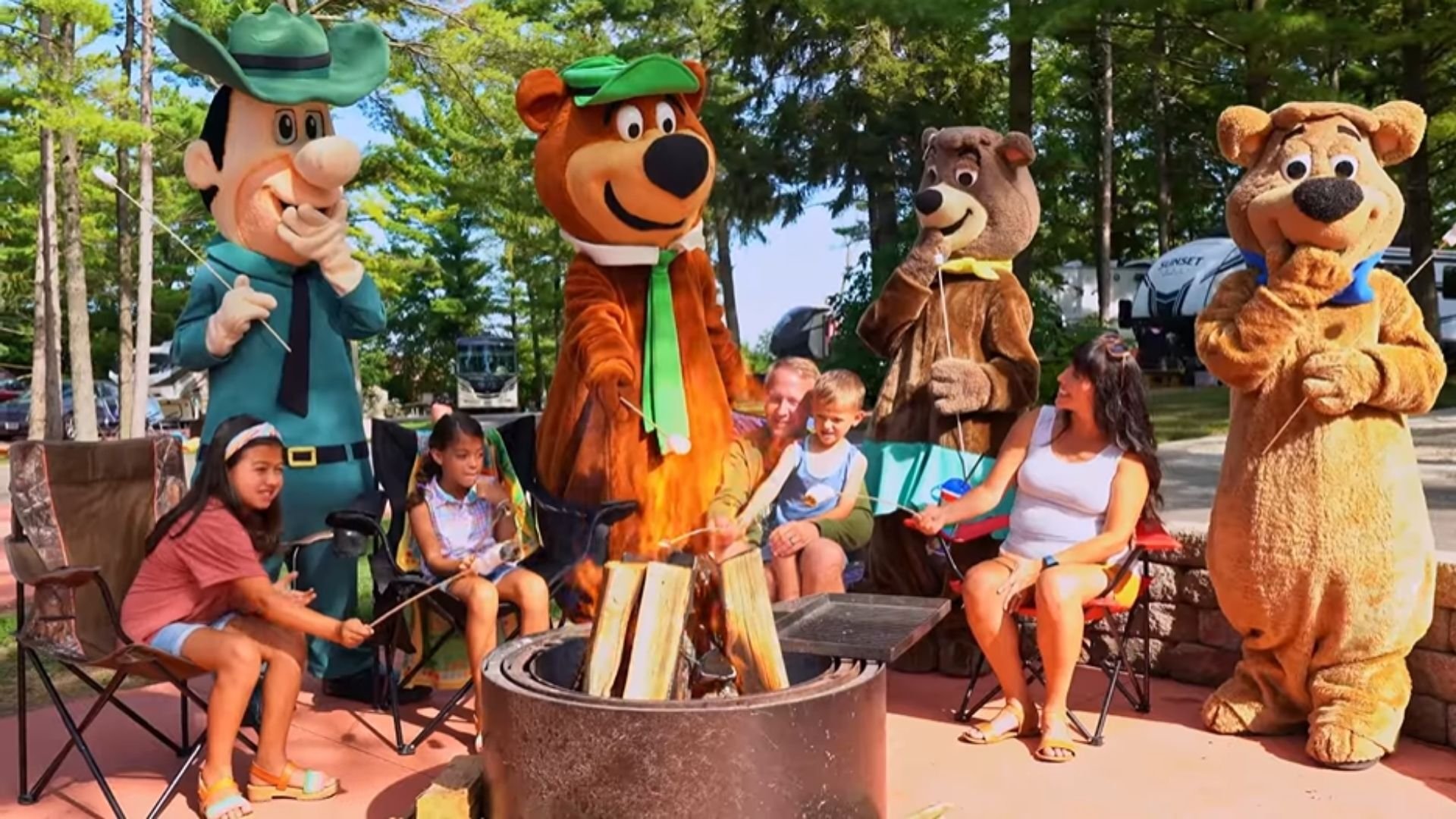 An image of a family of campers making s'mores with the mascots.