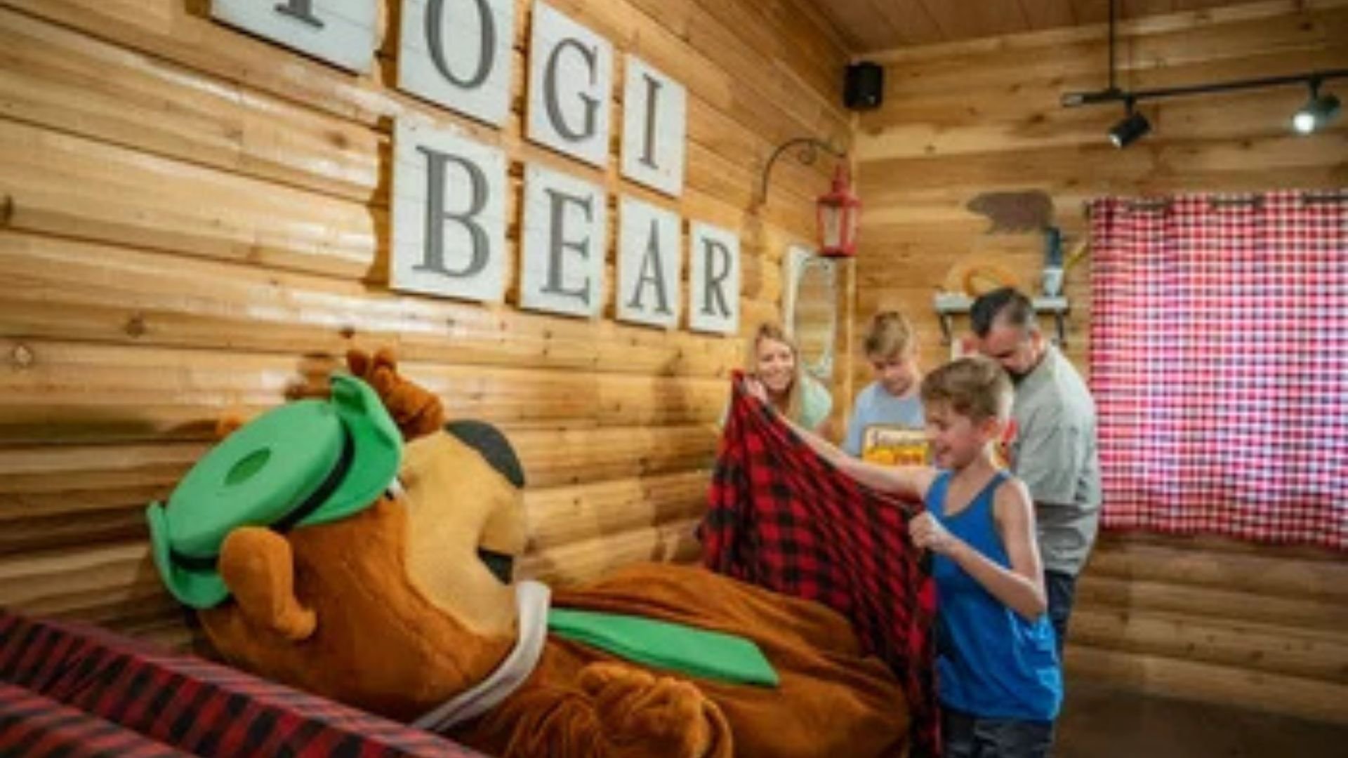 An image depicting a Jellystone Park-camping family tucking in Yogi Bear.