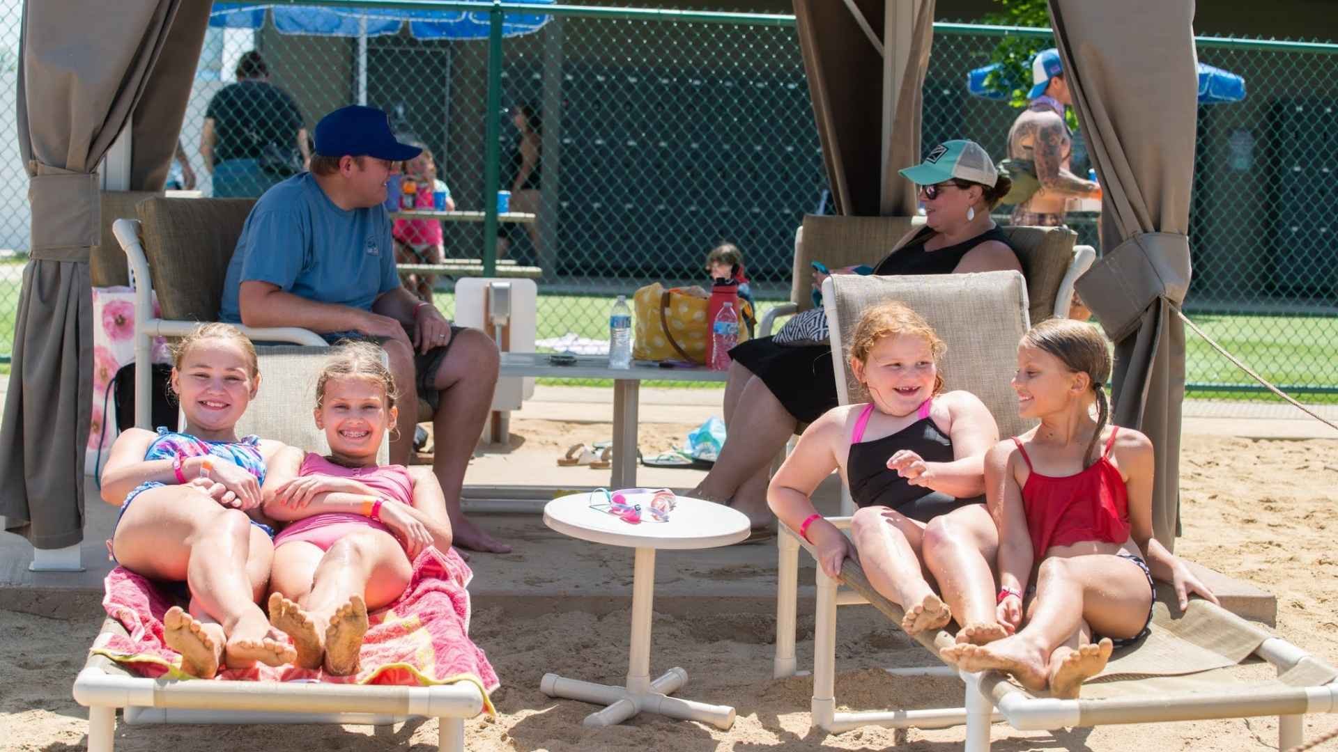 An image of some Jellystone campers lounging on one of the beach chairs outside of their parents' cabana at Bear Paw Beach.