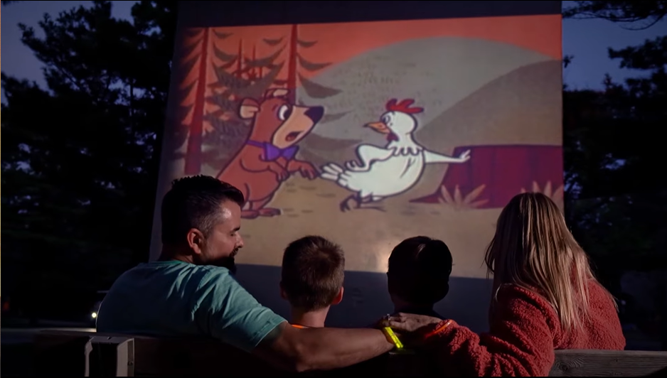 An image from Jellystone Park - Caledonia featuring a family relaxing at night and watching a show.