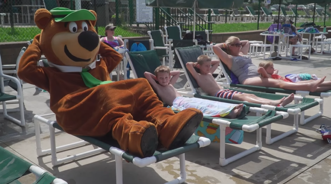 An image of Jellystone campers relaxing by the pool with Yogi Bear.