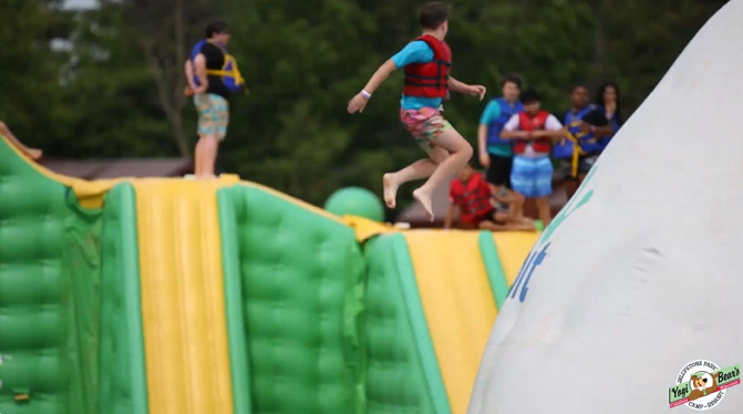 An image of a Jellystone camper jumping off of the Wibit into the water at Bear Paw Beach.
