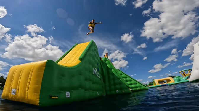 An image from Jellystone Park - Caledonia depicting a guest jumping off of the Wibit into the water at Bear Paw Beach