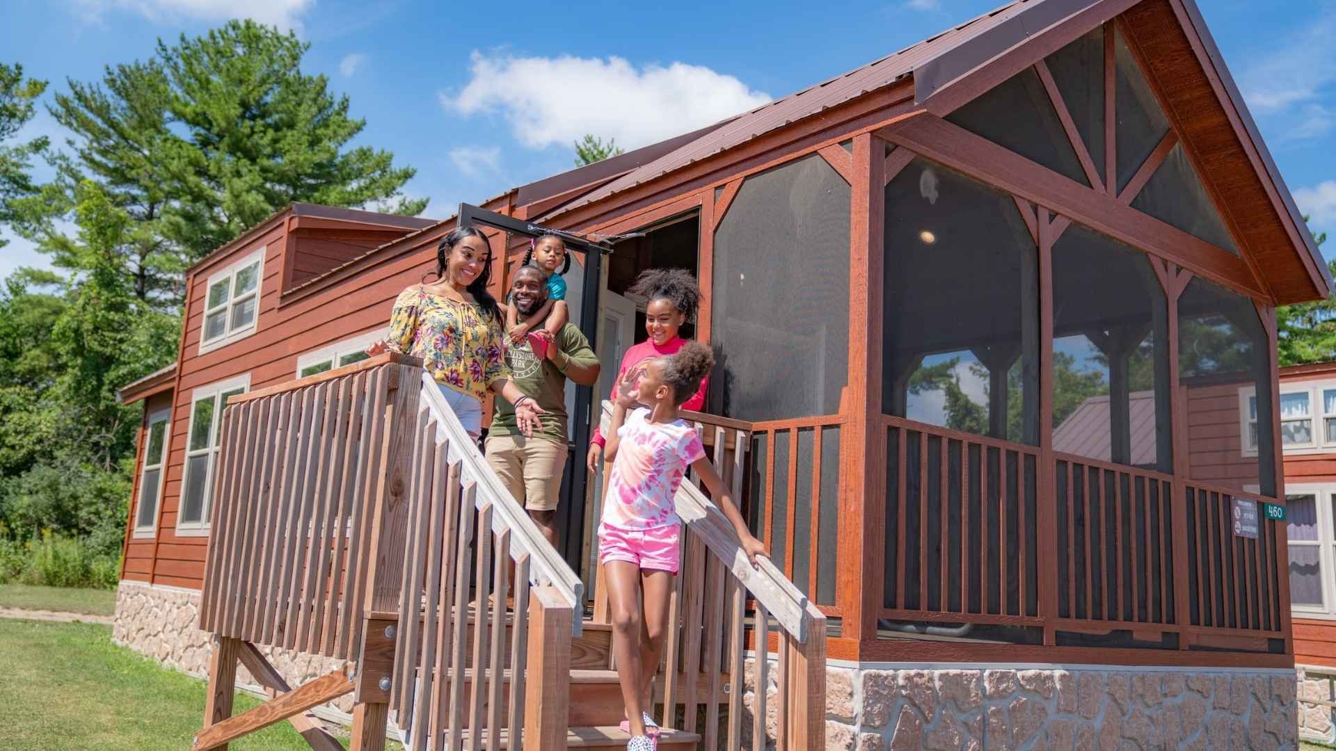 An image of a family standing on the stairs of their cabin at Jellystone Park.