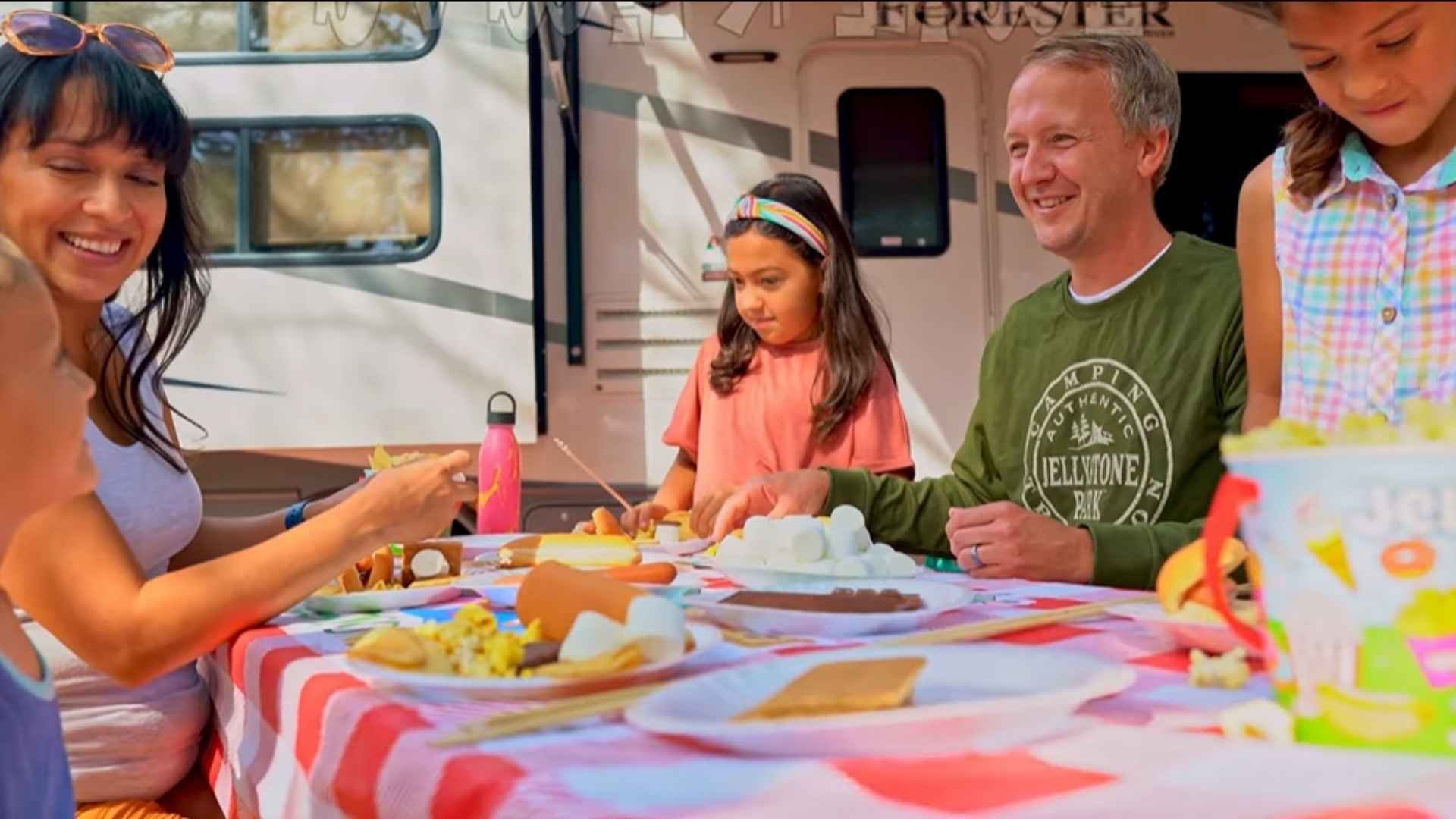 An image of a family of Jellystone campers eating dinner at their RV.