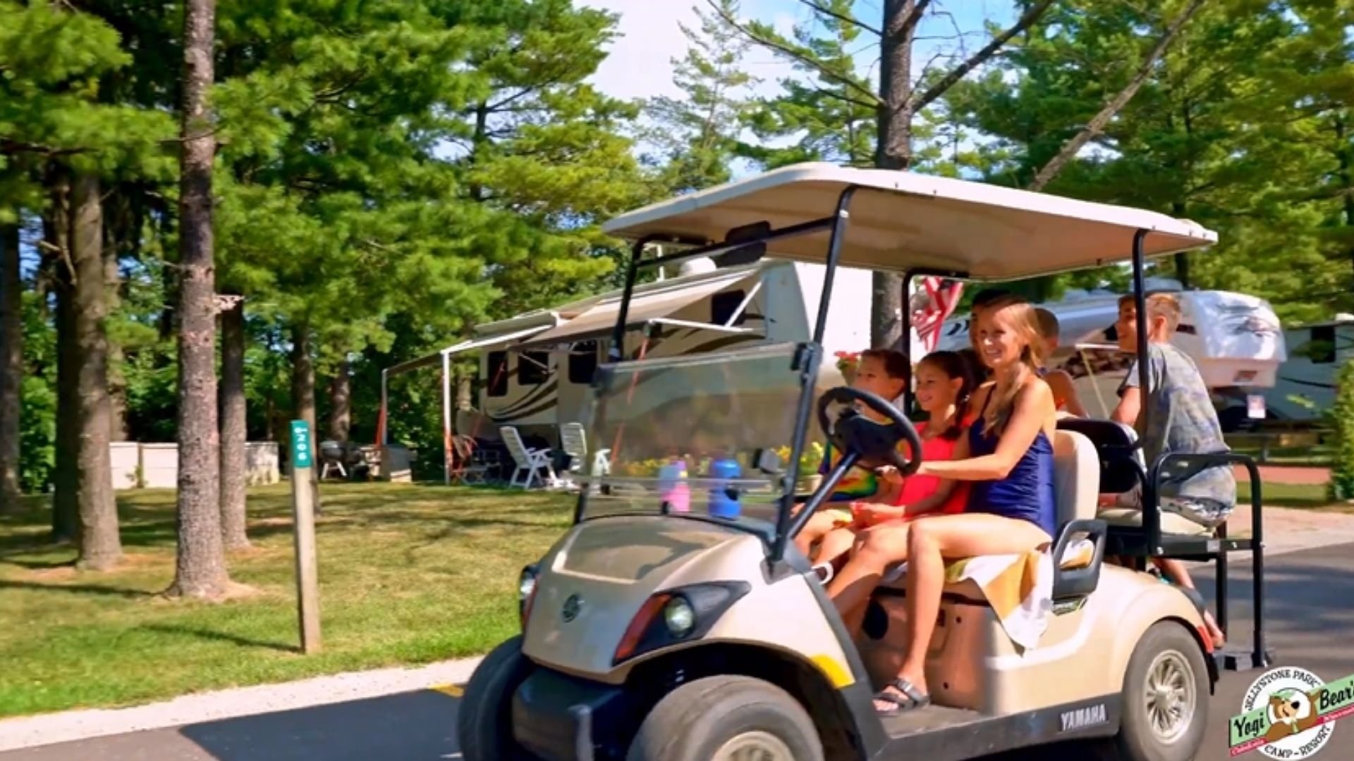 An image of a family at Jellystone Park riding to the Bear Paw Adventure Park attractions on a golf cart. An image of a family at Jellystone Park riding to the Bear Paw Adventure Park attractions on a golf cart.