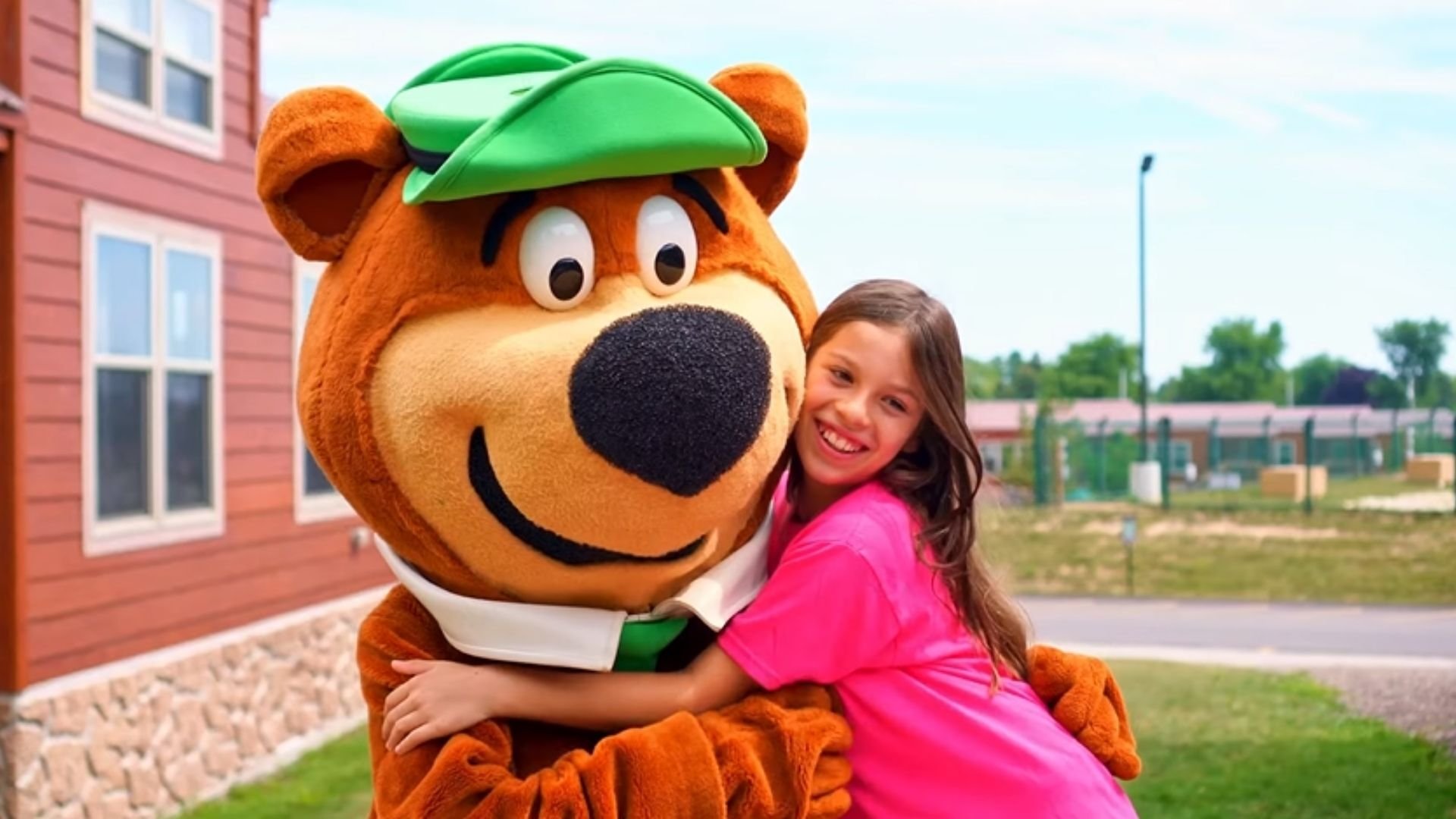 A Jellystone Park camper hugging Yogi Bear outside of her cabin. A Jellystone Park camper hugging Yogi Bear outside of her cabin.