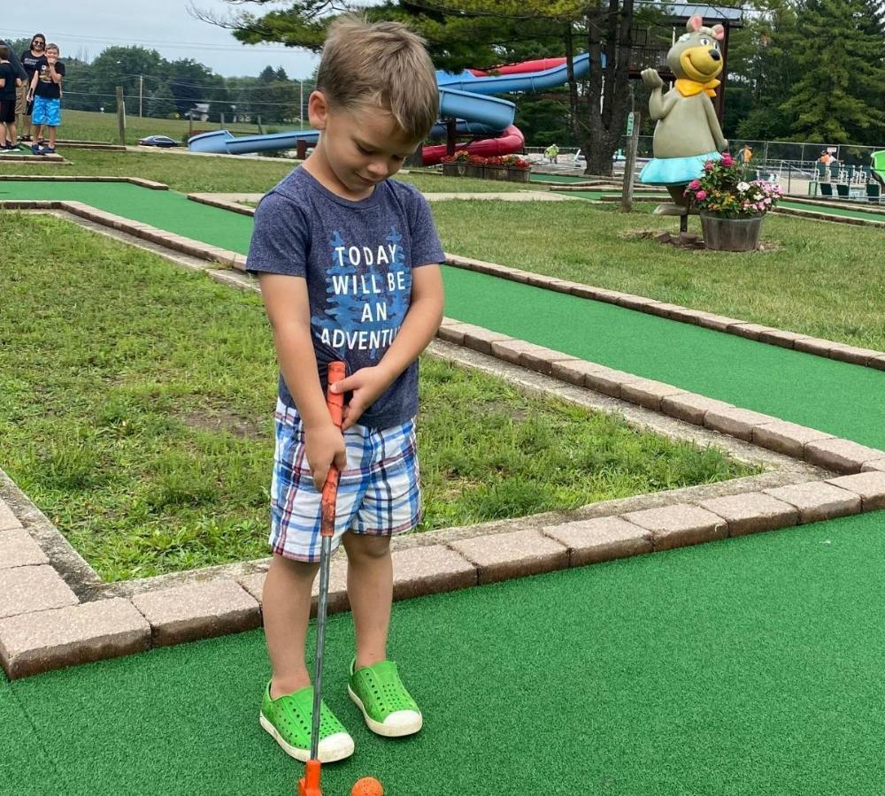 An image of a boy putting on the mini golf course at Jellystone Park™ Caledonia.